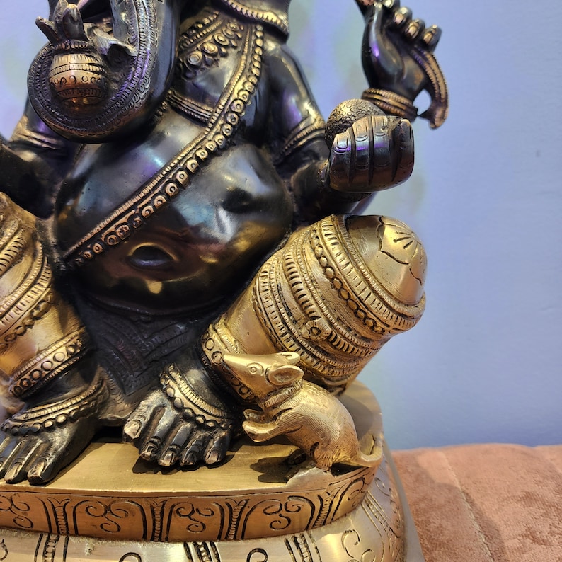 May include: A black and gold metal statue of Ganesha, the Hindu god of wisdom and prosperity. The statue is intricately detailed and features a rat at the base.