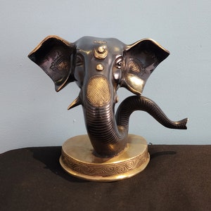 May include: A black and gold Ganesha statue with a curled trunk. The statue is on a round base with intricate details.
