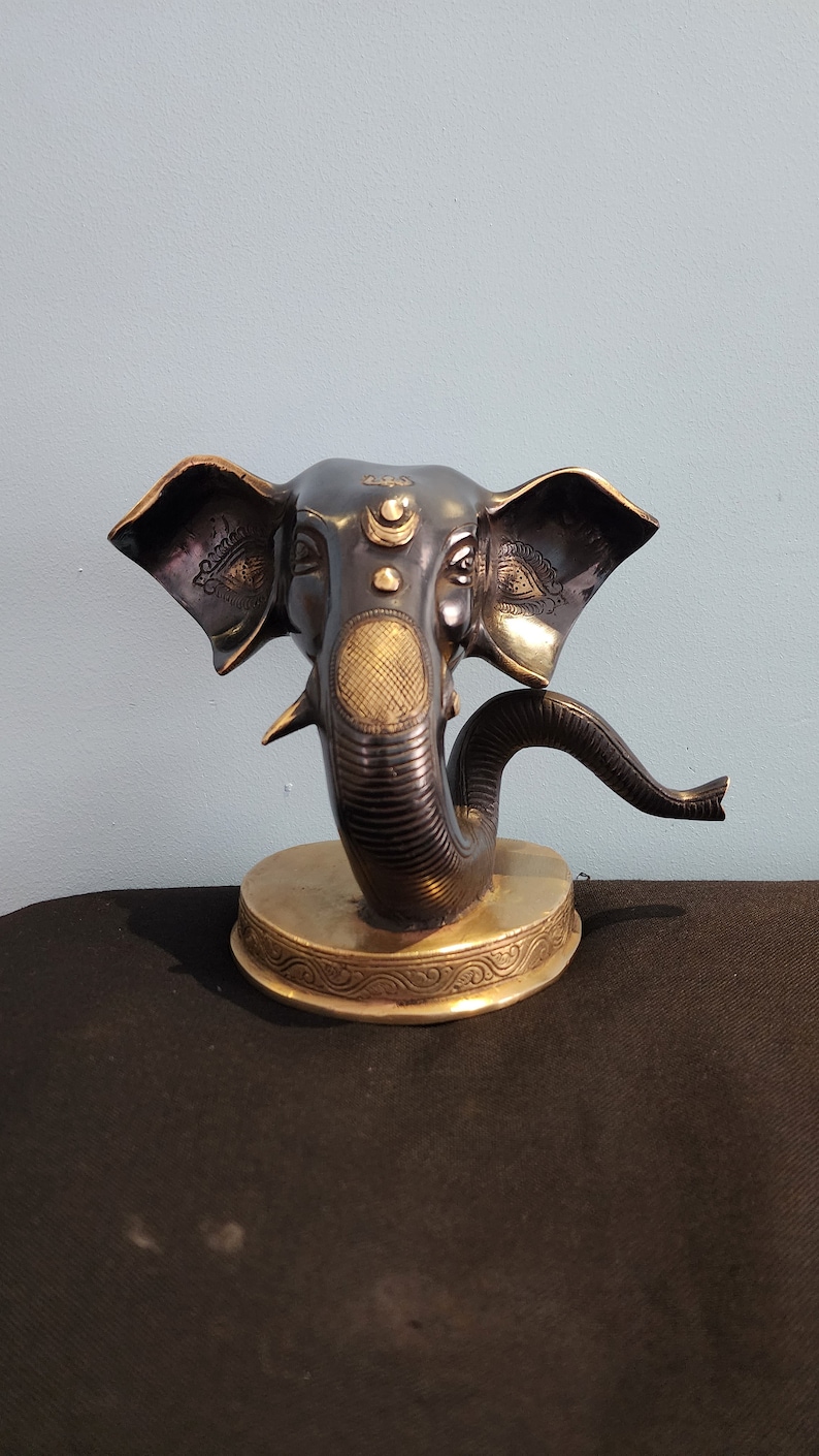 May include: A black and gold Ganesha statue with a curled trunk. The statue is on a round base with intricate details.