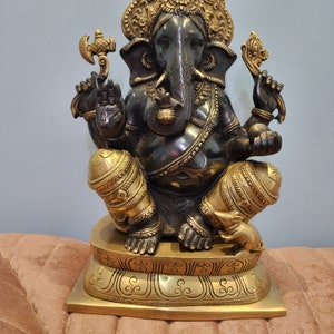 May include: A black and gold Ganesha statue with a decorative base. The statue is sitting on a brown surface.
