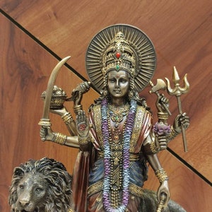 May include: A bronze statue of the Hindu goddess Durga, depicted with multiple arms and riding a lion. She is adorned with intricate jewelry and a garland of flowers.