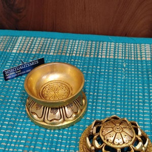 May include: Gold metal incense burner with a lotus flower design. The burner has a round base and a removable lid. The lid has a decorative design with holes for the incense to burn through.