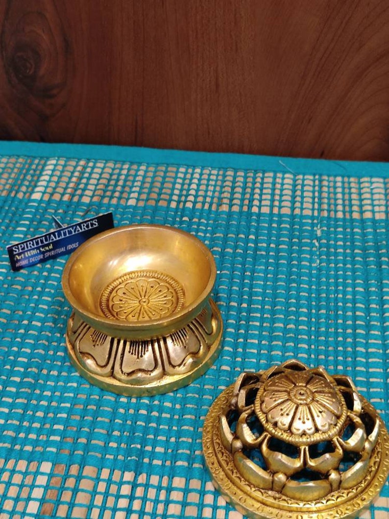 May include: Gold metal incense burner with a lotus flower design. The burner has a round base and a removable lid. The lid has a decorative design with holes for the incense to burn through.