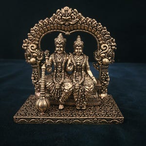May include: Gold-toned metal statue of a couple sitting under an ornate archway. The statue is detailed with intricate carvings and features a traditional Indian design.
