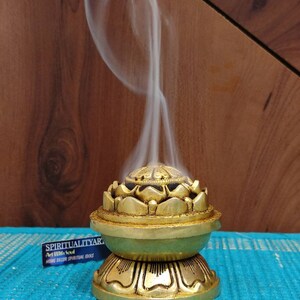May include: A gold metal incense burner shaped like a lotus flower with a round base. Smoke is rising from the top of the burner.