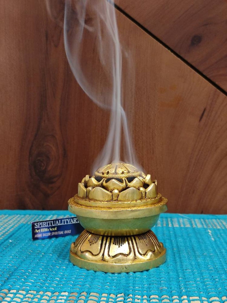 May include: A gold metal incense burner shaped like a lotus flower with a round base. Smoke is rising from the top of the burner.