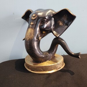 May include: A black and gold Ganesha statue with intricate details. The statue is made of metal and has a round base. The elephant's trunk is curled up and its eyes are closed.