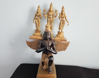 May include: A black kneeling statue of a deity with gold wings and a gold base. The statue is surrounded by three smaller gold statues of deities on individual bases.