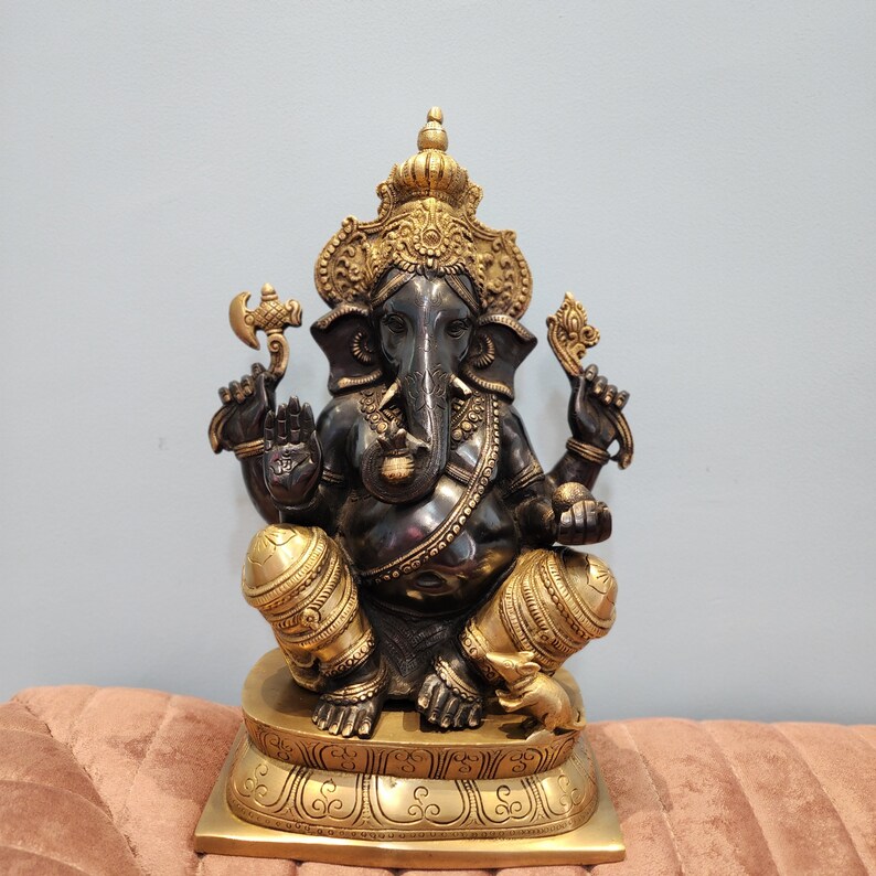 May include: A black and gold Ganesha statue with a decorative base. The statue is sitting on a brown surface.