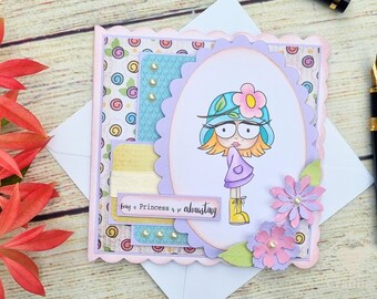 May include: A handmade greeting card with a cartoon illustration of a girl wearing a hat and boots. The card features a scalloped edge and decorative paper layers in pastel colours. Text on the card reads "being a Princess is exhausting."