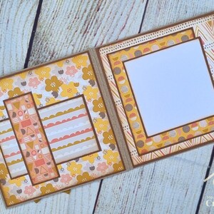 Peut inclure: Une mise en page de scrapbooking faite &agrave; la main avec deux pages ouvertes bord&eacute;es de papier cartonn&eacute; marron. La page de gauche pr&eacute;sente un motif floral avec des fleurs jaunes et roses, tandis que la page de droite comporte un grand cadre carr&eacute; blanc.