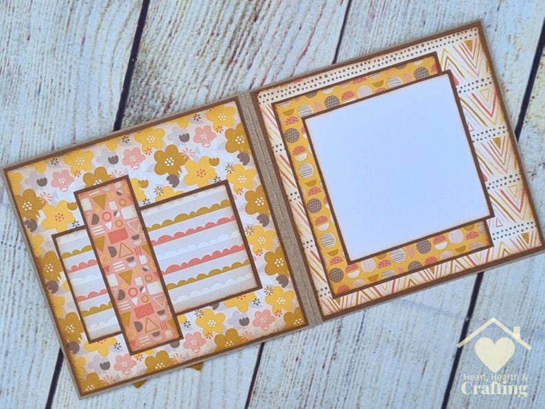 Peut inclure: Une mise en page de scrapbooking faite &agrave; la main avec deux pages ouvertes bord&eacute;es de papier cartonn&eacute; marron. La page de gauche pr&eacute;sente un motif floral avec des fleurs jaunes et roses, tandis que la page de droite comporte un grand cadre carr&eacute; blanc.