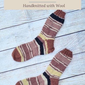 May include: A pair of hand-knitted wool socks featuring horizontal stripes in shades of brown, cream, yellow, and black. The text at the top reads Soft and Snuggly Coffee Socks Handknitted with Wool, and the bottom text reads www.hearthearthcrafts.com.
