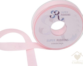 May include: A roll of pale pink ribbon with the text "SUPER RIBBONS COLLECTION" on the label. The ribbon is unrolled, revealing its smooth texture. The roll is in a clear plastic container.