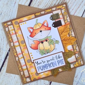 Peut inclure: Une carte de v&oelig;ux carr&eacute;e illustrant un renard de dessin anim&eacute; portant un chapeau citrouille et assis derri&egrave;re une citrouille. La carte porte l'inscription "You're sweet like PUMPKIN PIE" et est orn&eacute;e de papier &agrave; motifs automnaux et de feuilles.