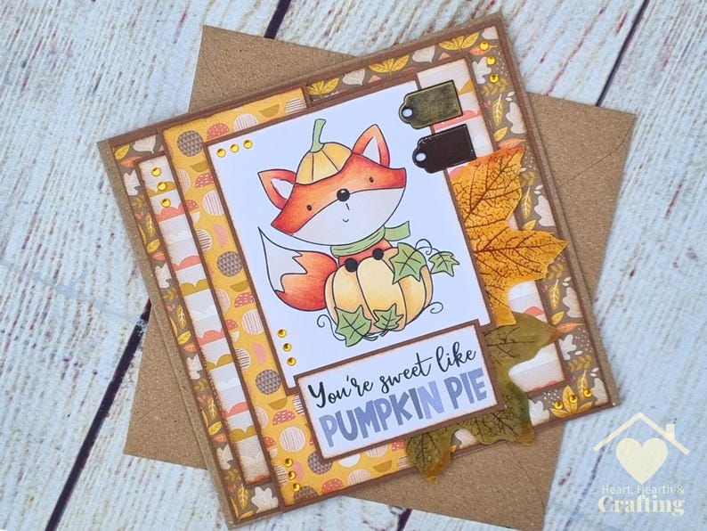 Peut inclure: Une carte de v&oelig;ux carr&eacute;e illustrant un renard de dessin anim&eacute; portant un chapeau citrouille et assis derri&egrave;re une citrouille. La carte porte l'inscription "You're sweet like PUMPKIN PIE" et est orn&eacute;e de papier &agrave; motifs automnaux et de feuilles.