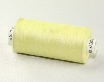 May include: A spool of pale yellow thread. The thread is tightly wound around a cylindrical core. The spool has white labels with the text "Coats Moon" and "BM 922071".