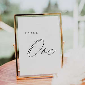 May include: A gold-framed table number sign with the word "TABLE" and the number "One" written in cursive script.