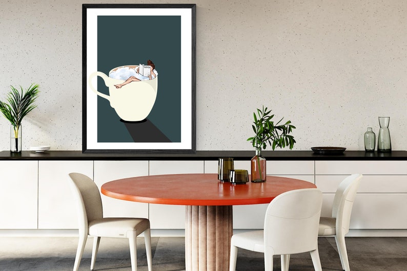 May include: A framed illustration of a woman relaxing in a cup of coffee, reading a book. The cup is white with a dark blue background.