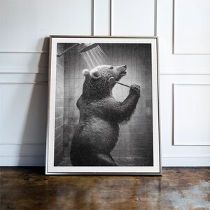 May include: A black and white photograph of a bear taking a shower. The bear is standing in a shower stall and holding a shower head. The bear is looking up at the shower head.
