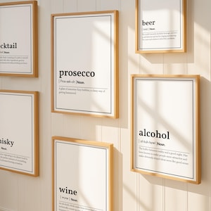May include: A collection of framed art prints with definitions of alcoholic beverages. Each print features a black font on a white background, with a wooden frame. The words include "cocktail", "prosecco", "whisky", "wine", "beer", and "alcohol".