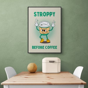 Może przedstawiać: Zielony i biały kresk&oacute;wkowy kubek do kawy z kwaśną miną i uniesionymi ramionami. Pod kubkiem znajduje się napis "STROPPY BEFORE COFFEE".
