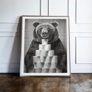 May include: A black and white photograph of a bear holding a stack of toilet paper rolls in front of a tiled wall.