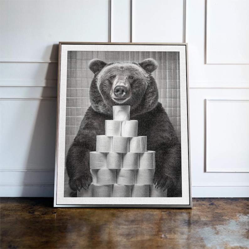 May include: A black and white photograph of a bear holding a stack of toilet paper rolls in front of a tiled wall.