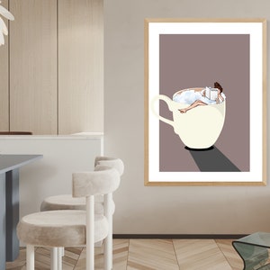 May include: A framed illustration of a woman relaxing in a large white coffee cup filled with foamy milk. The woman is reading a book and has her feet up. The background is a light brown color.