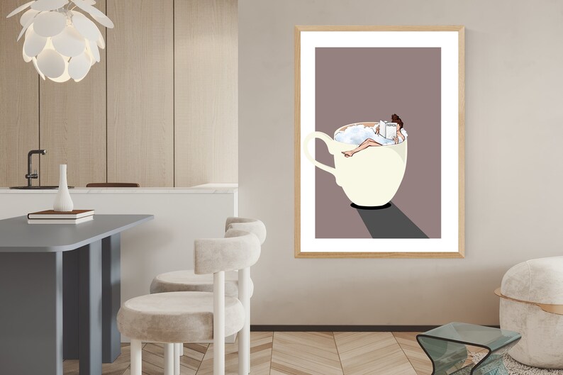 May include: A framed illustration of a woman relaxing in a large white coffee cup filled with foamy milk. The woman is reading a book and has her feet up. The background is a light brown color.