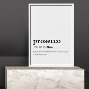 May include: A white framed print on a marble-look pedestal. The print features the word "prosecco" in a bold font, with a phonetic pronunciation and definition. The text below reads: "A glass of awesome fizzy bubbles, a classy way of getting hammered."