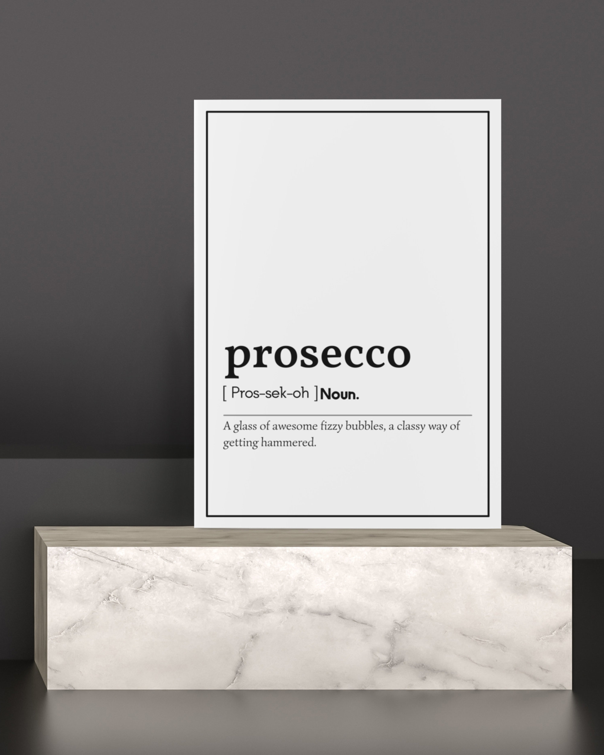 May include: A white framed print on a marble-look pedestal. The print features the word "prosecco" in a bold font, with a phonetic pronunciation and definition. The text below reads: "A glass of awesome fizzy bubbles, a classy way of getting hammered."