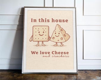 May include: Framed print with a beige background featuring a cartoon illustration of a smiling cracker and cheese wedge holding hands. The text "In this house" and "We love Cheese and crackers" is written in brown.