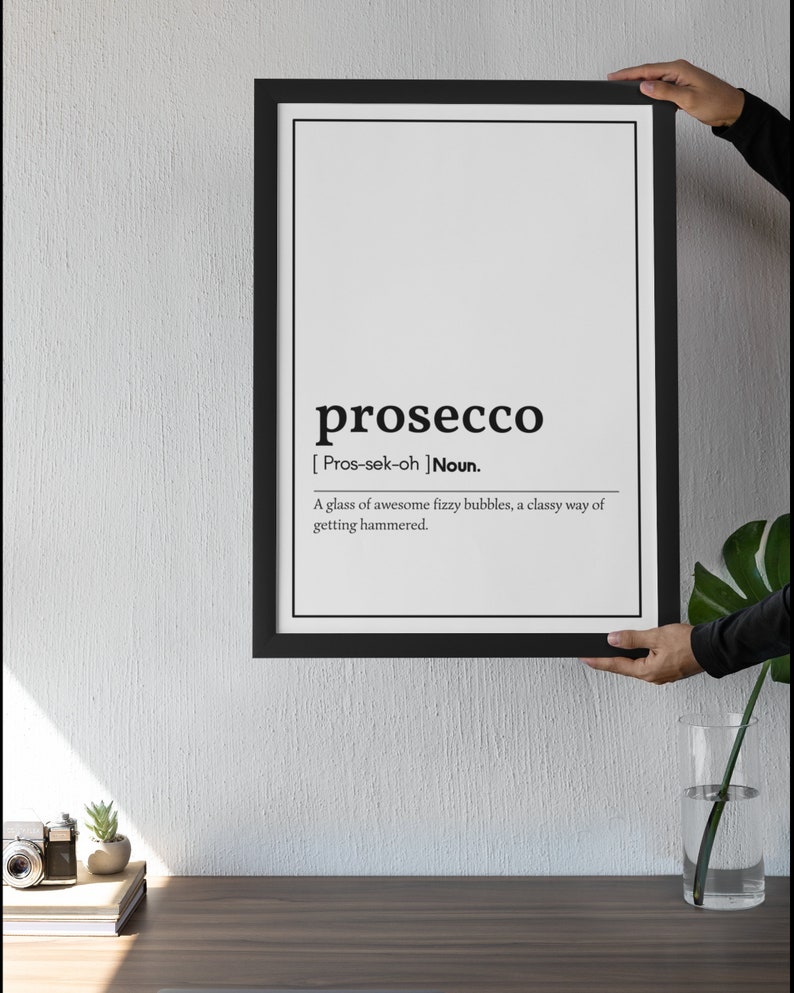 May include: A framed black and white print with the definition of "prosecco". The definition reads: "A glass of awesome fizzy bubbles, a classy way of getting hammered."