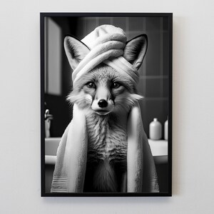 Puede incluir: Impresi&oacute;n en blanco y negro enmarcada de un zorro envuelto en una toalla blanca, con una toalla alrededor de la cabeza. El zorro est&aacute; en un entorno de ba&ntilde;o, con un lavabo y botellas en el fondo.