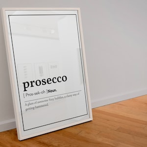 May include: A framed print with the word "prosecco" in a bold, black font. The definition below reads "A glass of awesome fizzy bubbles, a classy way of getting hammered." The frame is white, and the background is white.