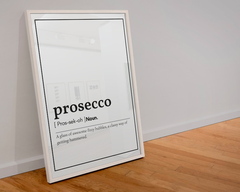 May include: A framed print with the word "prosecco" in a bold, black font. The definition below reads "A glass of awesome fizzy bubbles, a classy way of getting hammered." The frame is white, and the background is white.