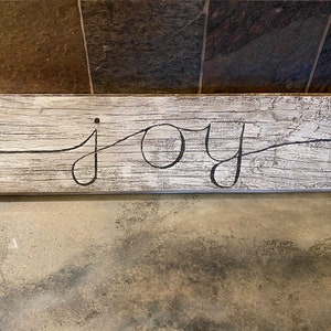 May include: A rustic wooden sign with the word "joy" written in black cursive lettering.