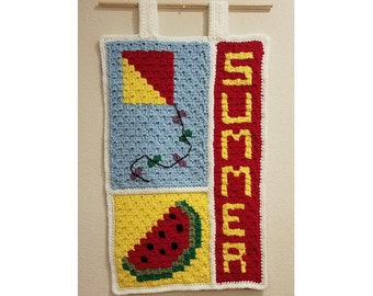 May include: A crocheted wall hanging with a blue, yellow, and red kite, a watermelon, and the word "SUMMER" in yellow letters on a red background.