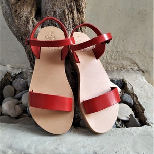 K&ouml;nnte beinhalten: Ein Paar rote Ledersandalen mit Schnallenverschluss. Die Sandalen haben ein schlichtes Design und sind aus hochwertigem Leder gefertigt.