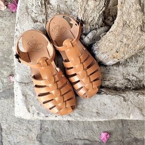 May include: A pair of light brown leather sandals with a cage-like design. The sandals have a strap around the ankle and the brand name "LEFOS" is visible on the insole. The sandals are size 8.