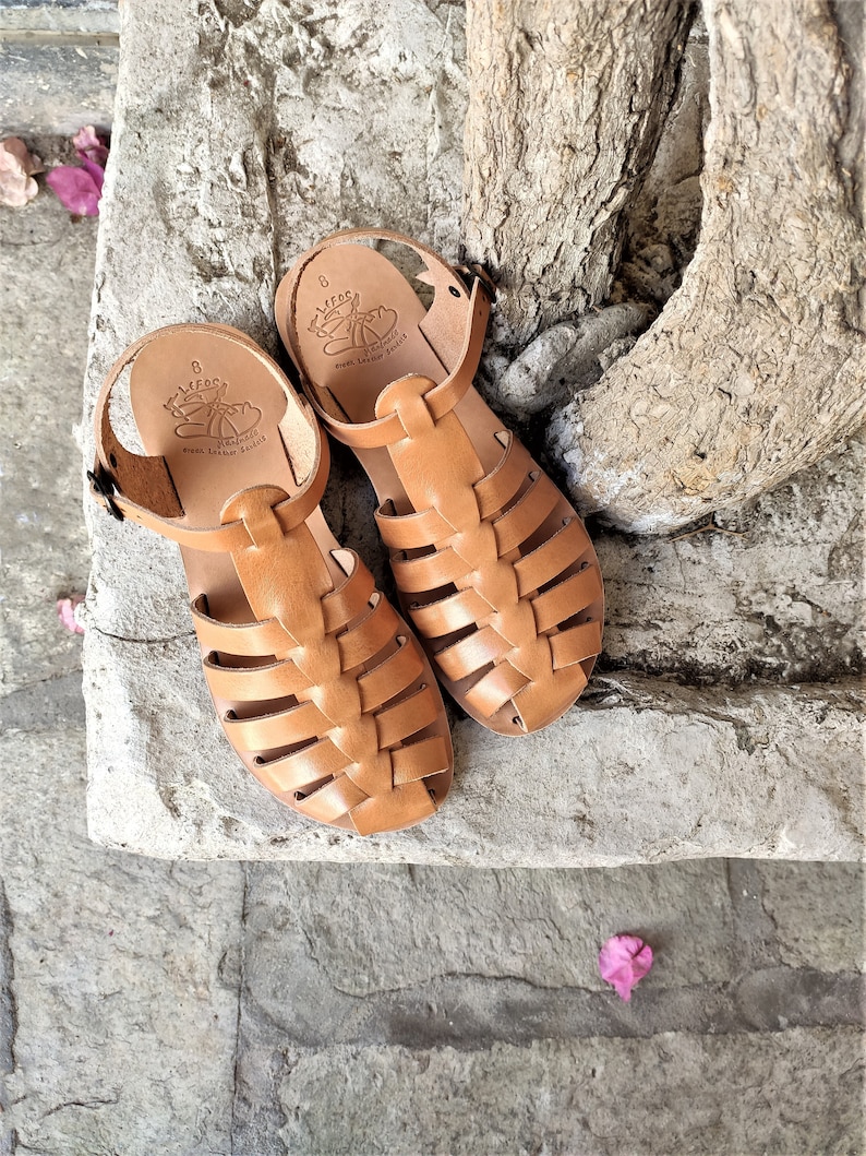 May include: A pair of light brown leather sandals with a cage-like design. The sandals have a strap around the ankle and the brand name "LEFOS" is visible on the insole. The sandals are size 8.
