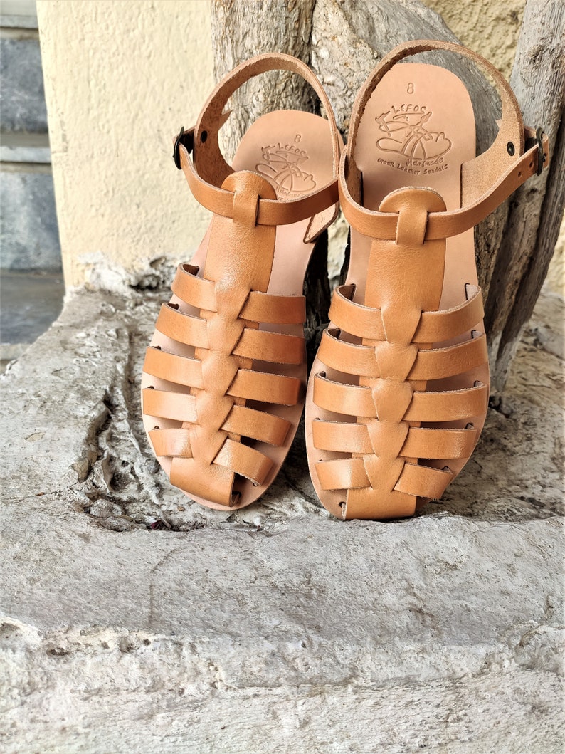 May include: A pair of light brown leather sandals with a woven design on the front. The sandals have ankle straps with buckles and are size 8. The sandals are handmade Greek leather sandals.