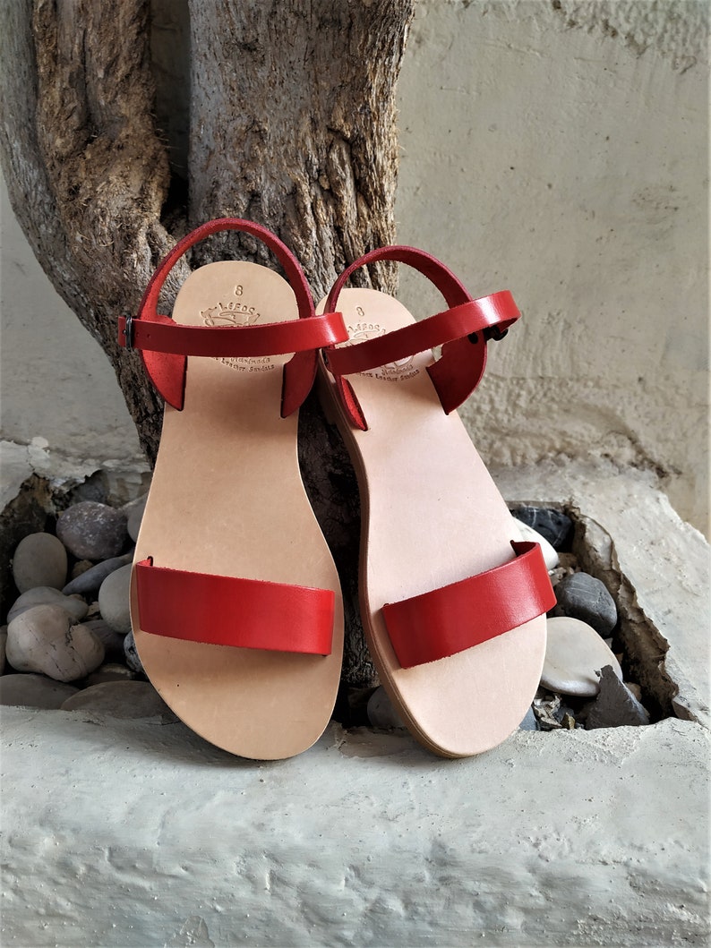 K&ouml;nnte beinhalten: Ein Paar rote Ledersandalen mit Schnallenverschluss. Die Sandalen haben ein schlichtes Design und sind aus hochwertigem Leder gefertigt.