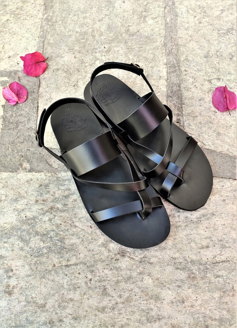 May include: A pair of black leather sandals with a criss-cross strap design. The sandals have a buckle fastening and a toe loop.