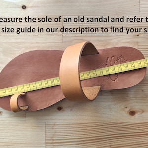 May include: A brown leather sandal with a yellow measuring tape across the sole. The tape measures 24 cm in length. The sandal has a strap that goes around the ankle and a toe loop.