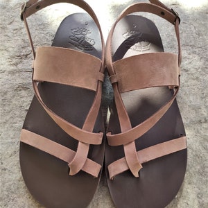 May include: A pair of brown leather sandals with a criss-cross strap design. The sandals have a buckle fastening and a comfortable footbed.