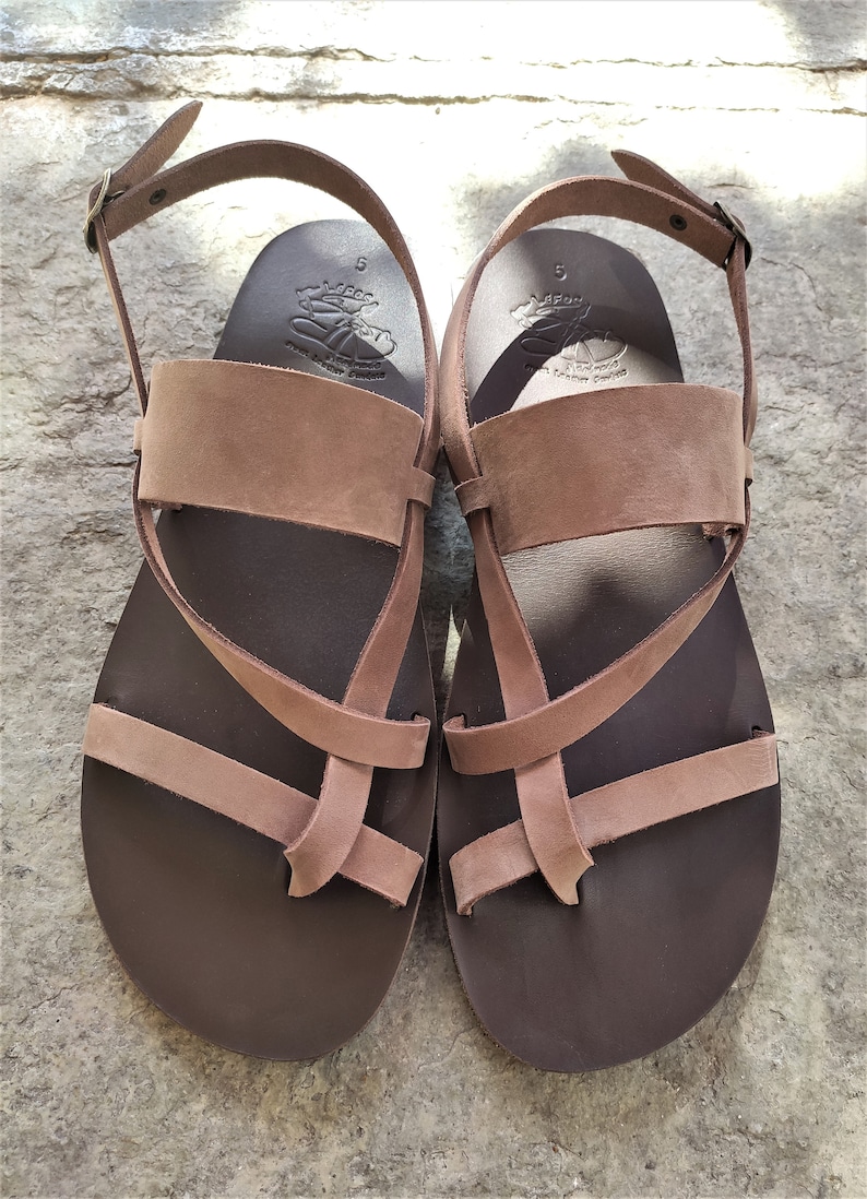 May include: A pair of brown leather sandals with a criss-cross strap design. The sandals have a buckle fastening and a comfortable footbed.