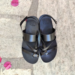 May include: Black leather sandals with a criss-cross strap design. The sandals have a buckle fastening and a comfortable footbed.