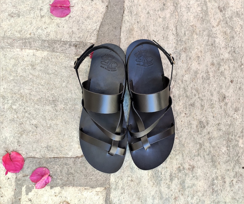 May include: Black leather sandals with a criss-cross strap design. The sandals have a buckle fastening and a comfortable footbed.